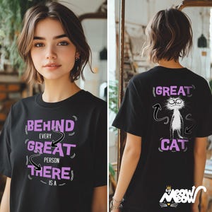 Puede incluir: Camiseta negra con un gr&aacute;fico morado que dice "Behind every great person there is a great cat". La parte posterior de la camiseta tiene un gato de dibujos animados con el texto "Great Cat" en morado.