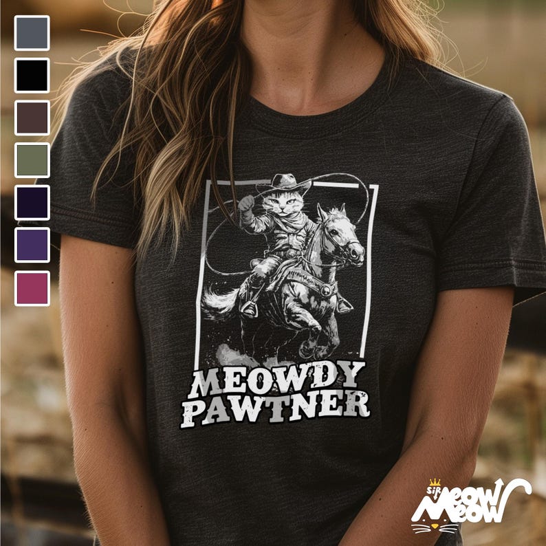 Pode incluir: Uma camiseta preta com um gr&aacute;fico branco de um gato usando um chap&eacute;u de cowboy e montando um cavalo. O texto "MEOWDY PAWTNER" &eacute; impresso abaixo do gr&aacute;fico.