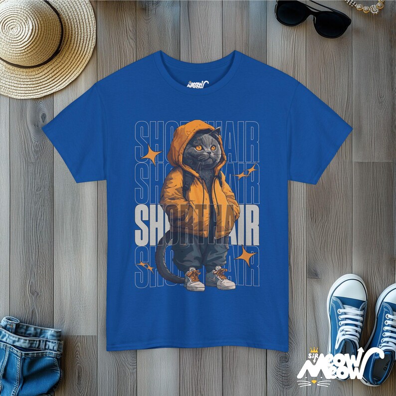 Humanized British Shorthair Cat standing up wearing a yellow hoodie and white and gray sneakers. Behind the cat is a stack of the word "Shorthair". The design appears on a woman wearing a royal blue tee.