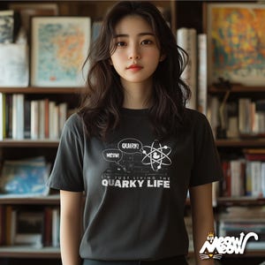 May include: A black t-shirt with a white graphic of an atom and speech bubbles that say "Meow!" and "Quark!" The text below the graphic says "I'm just living the quirky life."