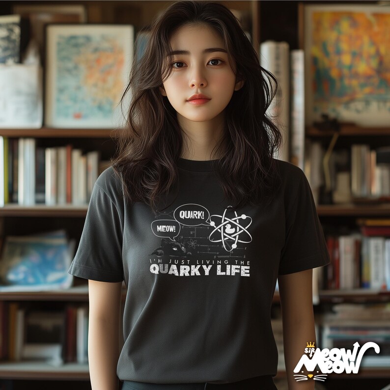 May include: A black t-shirt with a white graphic of an atom and speech bubbles that say "Meow!" and "Quark!" The text below the graphic says "I'm just living the quirky life."