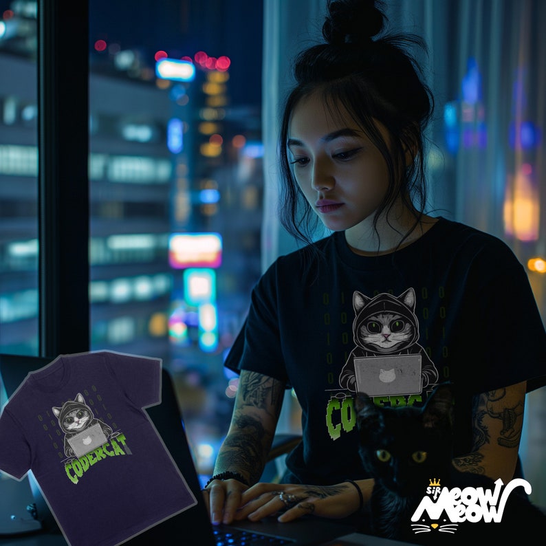 May include: A woman wearing a black t-shirt with a graphic of a cat wearing a hoodie and using a laptop. The text "CODERCAT" is printed on the shirt. The woman is sitting at a desk with a laptop in front of her. A black cat is sitting on the desk next to the woman.