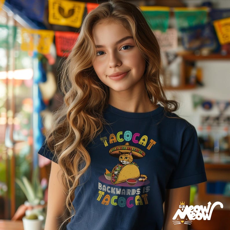 May include: A navy blue t-shirt with a colorful graphic of a cat wearing a sombrero and eating a taco. The text "Tacocat" is above the cat and "Backwards is Tacocat" is below the cat.