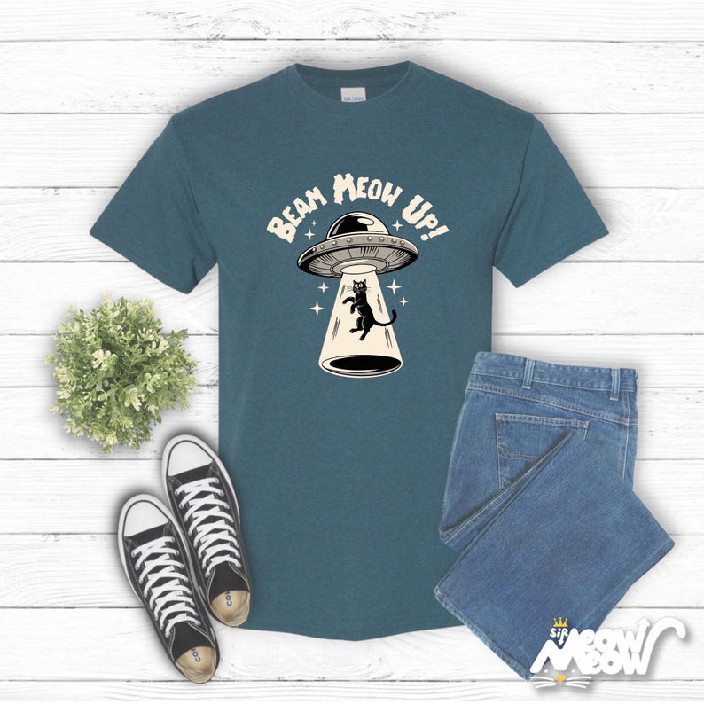 May include: A teal blue t-shirt with a black cat being beamed up by a UFO. The text on the shirt reads "Beam Meow Up!"