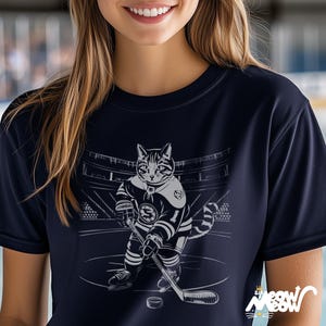 May include: A navy blue t-shirt with a graphic of a cat playing hockey. The cat is wearing a hockey jersey with the number 1 on it. The cat is holding a hockey stick and is skating on the ice. The graphic is in a vintage style.