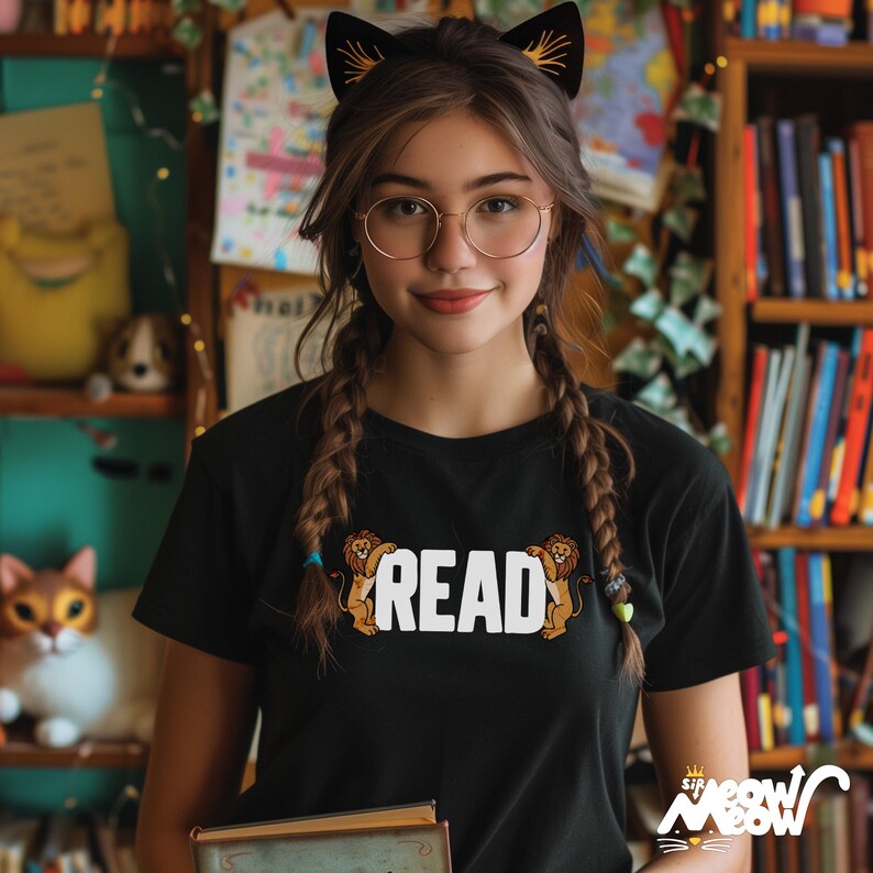 May include: A young person wearing a black t-shirt with the word "READ" printed on it, surrounded by two cartoon lions. The person is wearing round glasses and has their hair in two braids. They are holding a book in their hands.