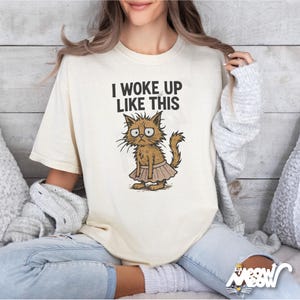 May include: A white t-shirt with the text "I woke up like this" and a cartoon illustration of a cat wearing a pink tutu.