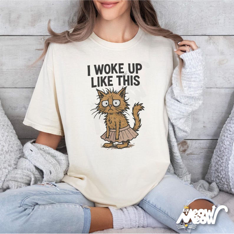 May include: A white t-shirt with the text "I woke up like this" and a cartoon illustration of a cat wearing a pink tutu.