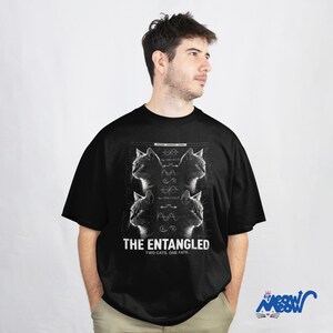 May include: Black t-shirt featuring a graphic with four cat portraits and scientific diagrams. The text "THE ENTANGLED TWO CATS. ONE FATE." is printed below the graphic. The shirt also has the "Sip Meow Meow" logo.