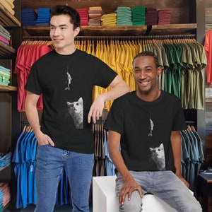May include: Two people wearing black t-shirts with a white cat and fish graphic. The cat is looking up at the fish on a fishing line. The t-shirts are on a black background.