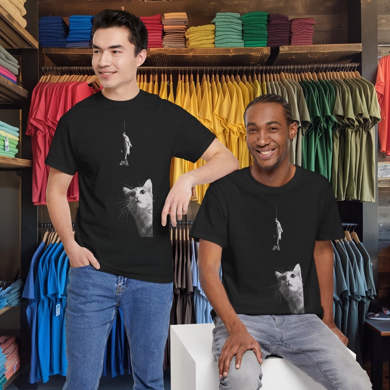 May include: Two people wearing black t-shirts with a white cat and fish graphic. The cat is looking up at the fish on a fishing line. The t-shirts are on a black background.