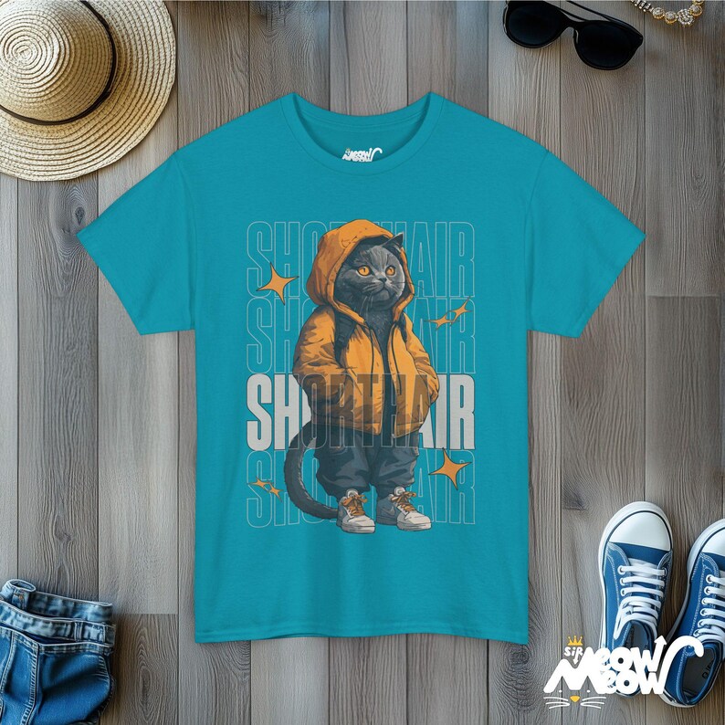 Humanized British Shorthair Cat standing up wearing a yellow hoodie and white and gray sneakers. Behind the cat is a stack of the word "Shorthair". The design appears on a woman wearing a tropical blue tee.