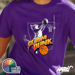 May include: Purple t-shirt with a white graphic of a cat dunking a basketball. The graphic says "Slam Dunk".