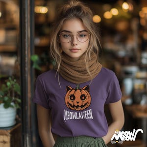 May include: A purple t-shirt with an orange and black jack-o'-lantern cat design and the text "MEOWLAWEEN". The shirt is part of a Halloween-themed collection.