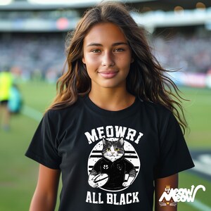 May include: A black t-shirt featuring a white graphic of a cat wearing a rugby jersey and holding a rugby ball. The text "MEOWRI ALL BLACK" is printed on the shirt.