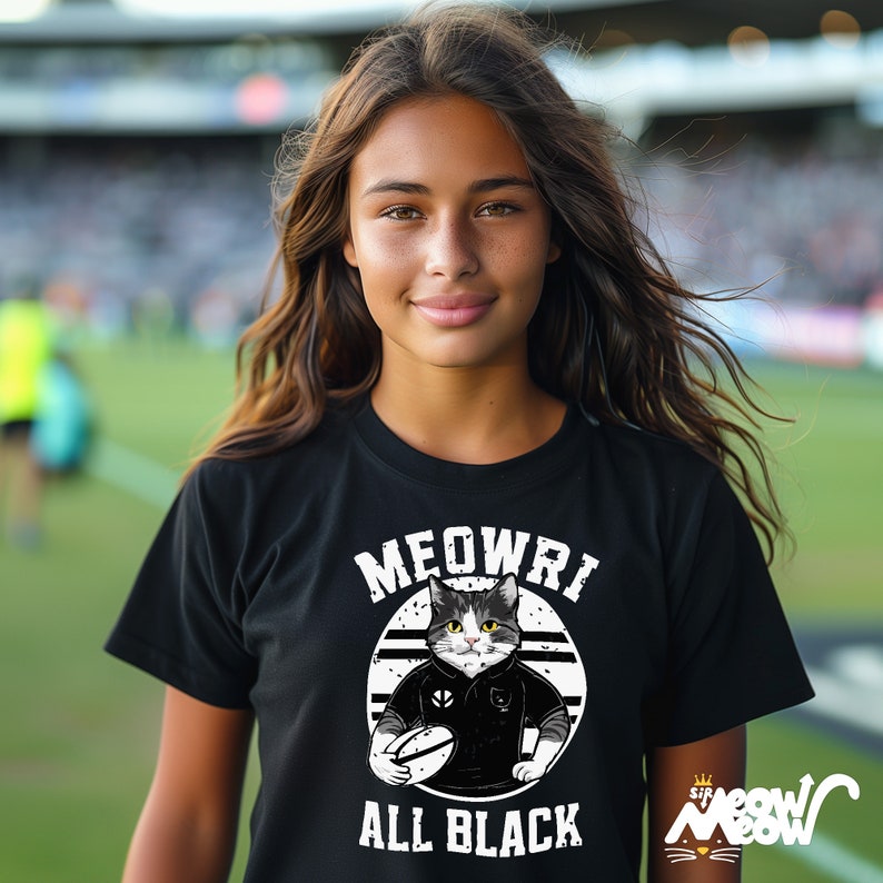 May include: A black t-shirt featuring a white graphic of a cat wearing a rugby jersey and holding a rugby ball. The text "MEOWRI ALL BLACK" is printed on the shirt.