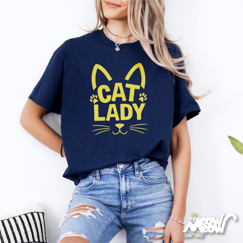 Peut inclure: Un t-shirt bleu marine avec un motif de chat jaune et le texte "CAT LADY".