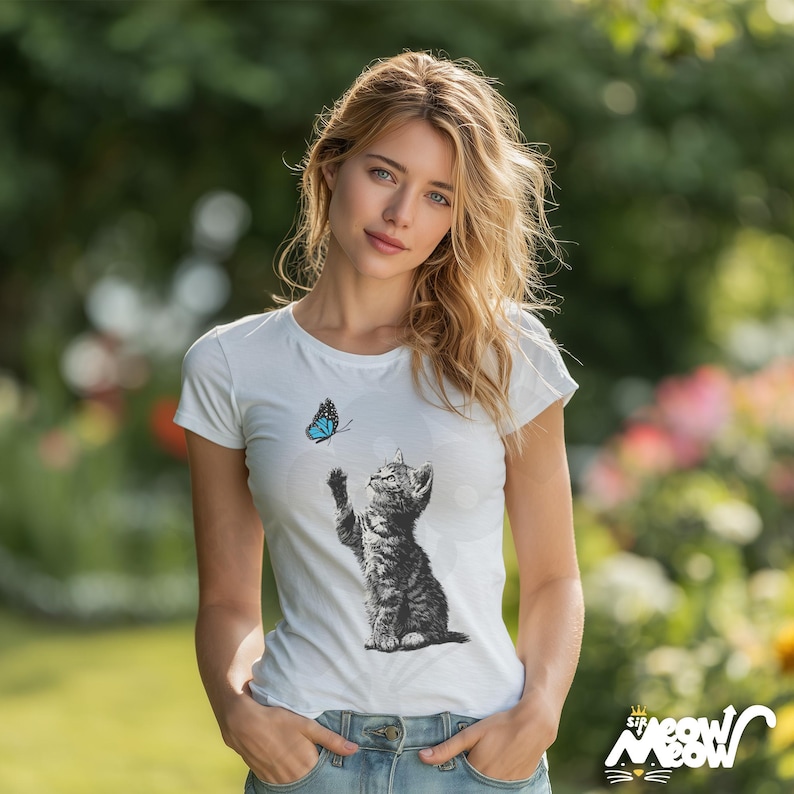 May include: White t-shirt featuring a black and white illustration of a kitten reaching for a blue butterfly. The shirt has the text "Sir Meow Meow" in a stylized font. The model is wearing blue jeans.