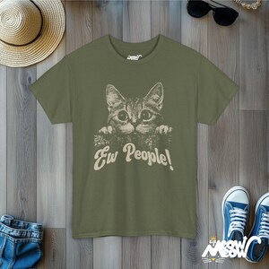 Puede incluir: Una camiseta verde con un gr&aacute;fico de un gato mirando por encima de una pared y el texto "Ew People!" impreso en la parte delantera.