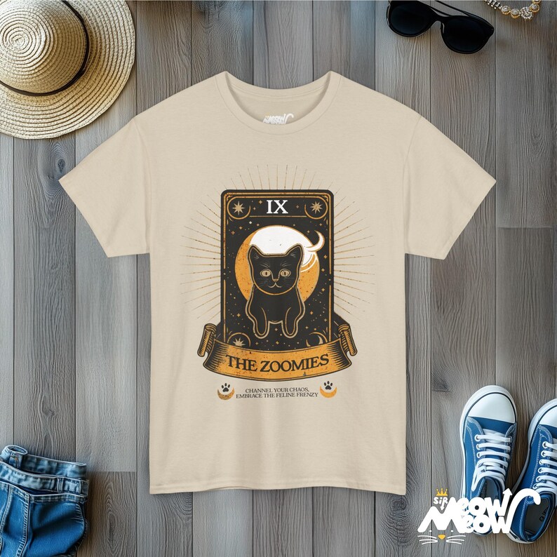 Puede incluir: Una camiseta beige con una ilustraci&oacute;n de un gato negro en estilo de carta de tarot. La carta est&aacute; etiquetada como "IX The Zoomies" y dice "Channel your chaos, embrace the feline frenzy".