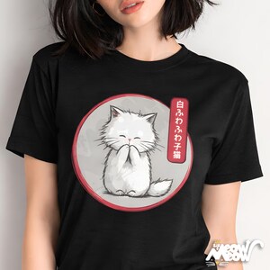 May include: Black t-shirt featuring a white cartoon cat with closed eyes and paws together, inside a red-rimmed circle. Japanese text is on the right. The cat is on a gray background. The shirt has a small logo at the bottom.