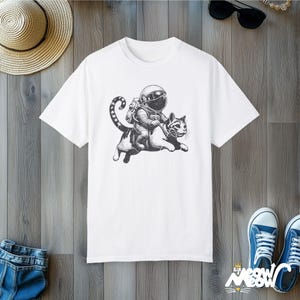 White Comfort Colors 1717 unisex T-shirt with a humorous white graphic of an astronaut riding atop a playful cat, combining outer space and cat lover themes.
