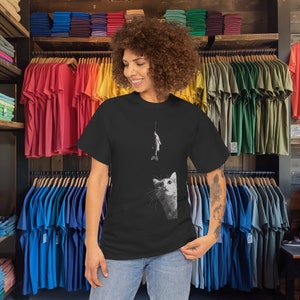 May include: A black t-shirt with a graphic of a cat looking up at a fish on a fishing line. The cat is white and the fish is gray.