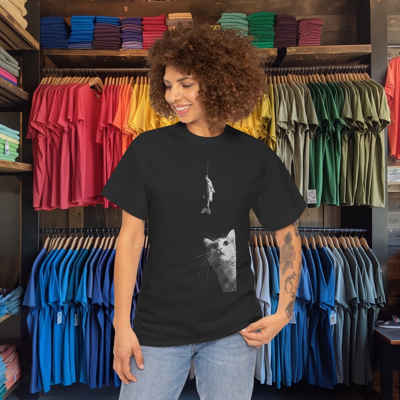 May include: A black t-shirt with a graphic of a cat looking up at a fish on a fishing line. The cat is white and the fish is gray.