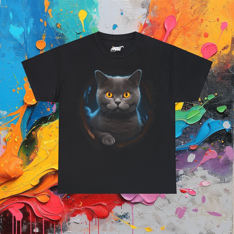 May include: Black t-shirt with a graphic of a gray cat with yellow eyes peeking out of a hole. The cat has a serious expression and is looking directly at the viewer.