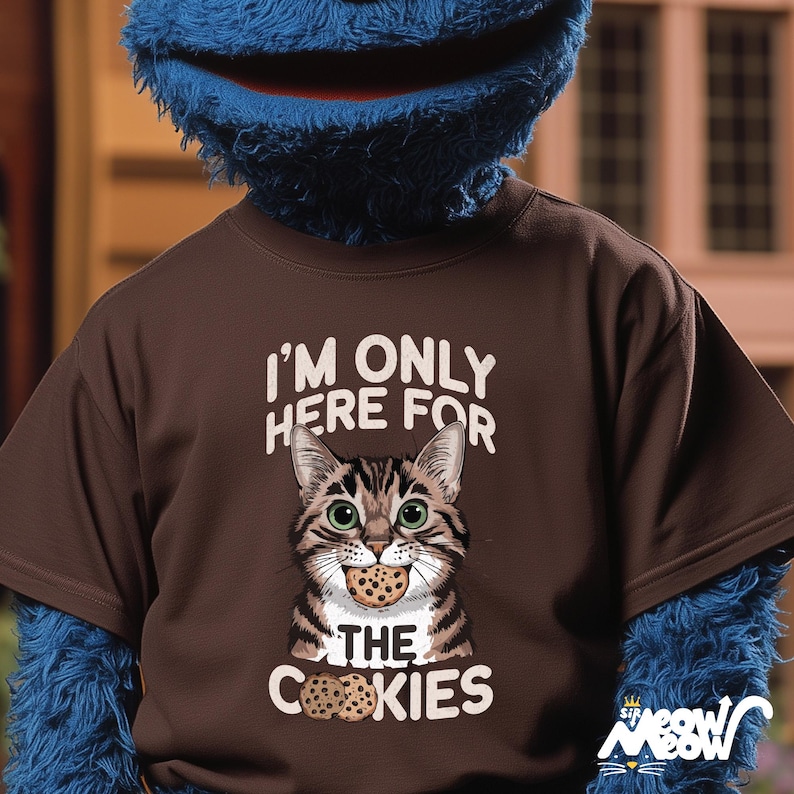 May include: Brown t-shirt with a cartoon cat wearing a cookie. The text on the shirt reads "I'm only here for the cookies".