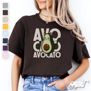 May include: A brown t-shirt with a white graphic of a cat inside an avocado. The text "Avo CATO" is printed below the avocado.