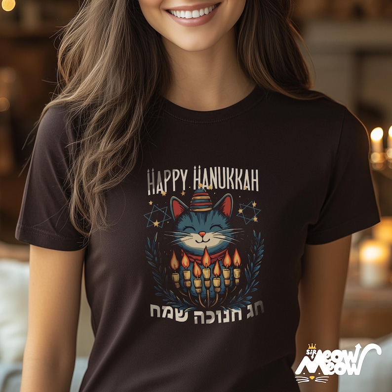 May include: A black t-shirt with a graphic of a cat wearing a hat and holding a menorah. The text "Happy Hanukkah" and Hebrew text are printed on the shirt.