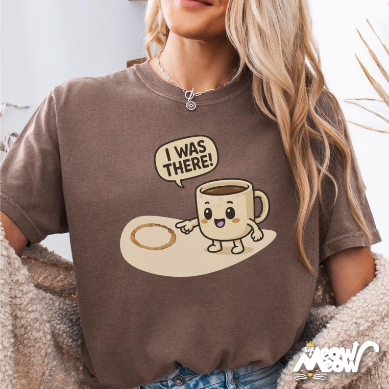 May include: A brown t-shirt with a cartoon coffee cup and the text "I was there!" The coffee cup is pointing to a coffee ring on the ground.