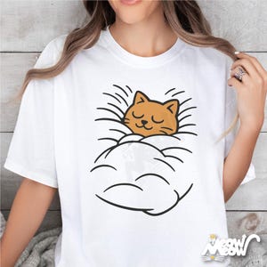 May include: White t-shirt featuring a cartoon cat sleeping in a cloud. The cat is orange with closed eyes, and the cloud is outlined in black. The shirt has the text "Meow Meow" in the bottom right corner.