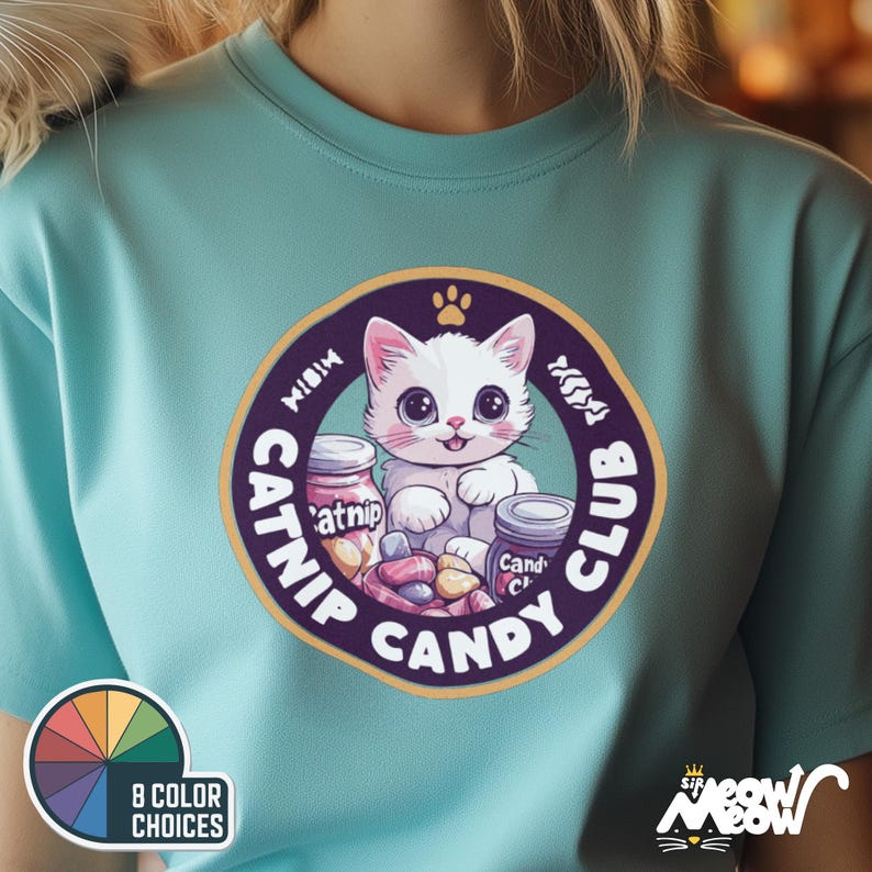 May include: A turquoise blue t-shirt with a white cat wearing a pink collar and holding a jar of catnip. The cat is surrounded by candy and the text "Meow Catnip Candy Club" in a purple circle.