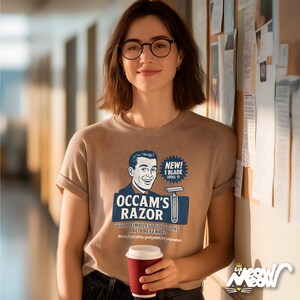 K&ouml;nnte beinhalten: Ein beiges T-Shirt mit dem Text "Occam's Razor" und einer Illustration eines Mannes und eines Rasierers. Das Shirt hat auch den Text "Wenn einfachste L&ouml;sungen bevorzugt werden". Die Person h&auml;lt eine rote Kaffeetasse.