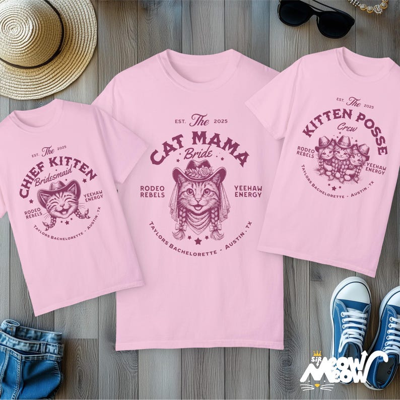 May include: Three pink t-shirts with cat-themed graphics. One shirt says "Cat Mama Bride," another says "Chief Kitten Bridesmaid," and the third says "Kitten Posse Crew." All shirts have a rodeo theme with text that reads "Rodeo Rebels" and "Yeehaw Energy."