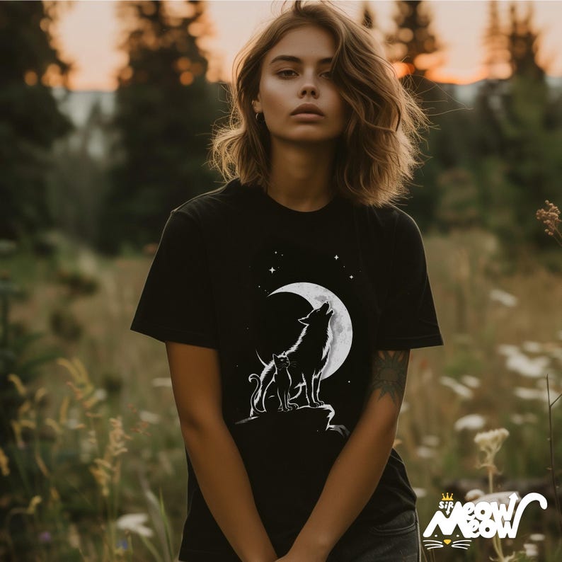 May include: Black t-shirt with a white graphic of a wolf howling at the moon with a cat beside it. The moon is a crescent shape with stars in the background.