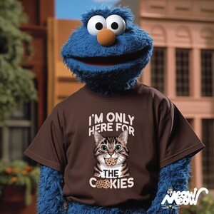 May include: A brown t-shirt with a cartoon cat wearing a cookie. The text on the shirt reads "I'm only here for the cookies".