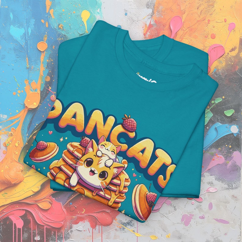 May include: A teal blue t-shirt with a graphic of two cartoon cats on a stack of pancakes. The text "PANCAKATS" is written in a playful font above the cats.