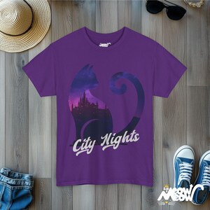 Pode incluir: Camiseta roxa com a silhueta de um gato com um horizonte urbano dentro do seu corpo. O texto "City Nights" est&aacute; impresso abaixo do gato.