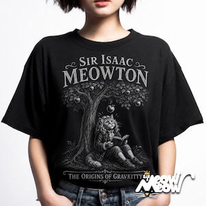 May include: A black t-shirt featuring a white graphic illustration of a cat dressed in 17th-century attire, sitting under an apple tree and reading a book. The text reads SIR ISAAC MEOWTON and THE ORIGINS OF GRAVKITTY in a stylized white font.