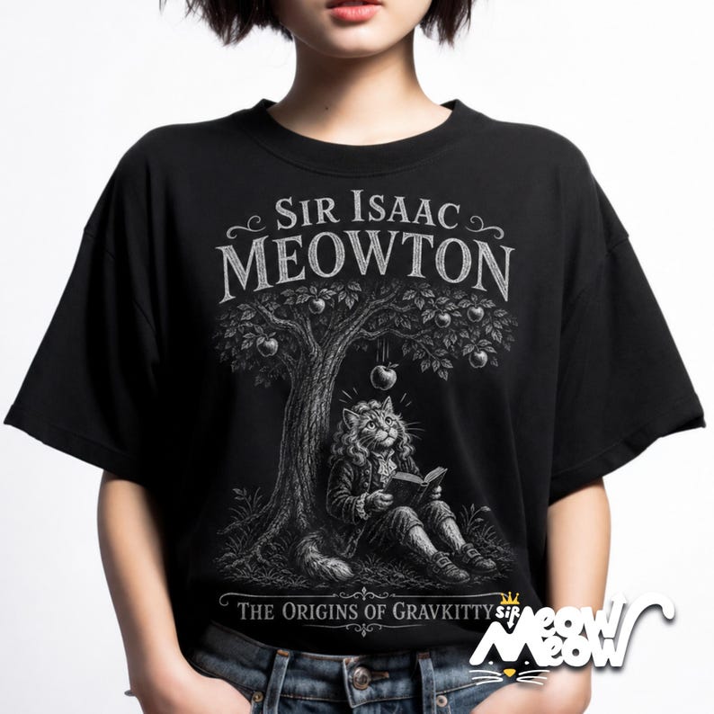 May include: A black t-shirt featuring a white graphic illustration of a cat dressed in 17th-century attire, sitting under an apple tree and reading a book. The text reads SIR ISAAC MEOWTON and THE ORIGINS OF GRAVKITTY in a stylized white font.