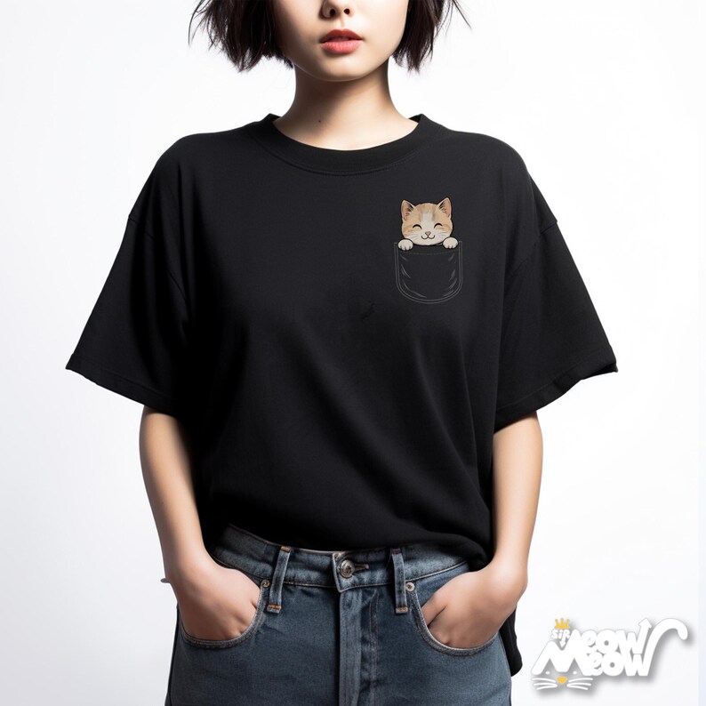 May include: Black t-shirt featuring a pocket with a cartoon cat peeking out. The cat has orange and white fur and a smiling expression. The shirt is a crew neck style and is made of a soft material.