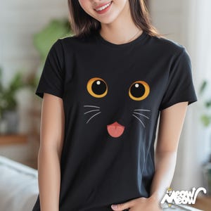 May include: Black t-shirt featuring a cartoon cat face with large yellow eyes, white whiskers, and a pink tongue. The shirt has a crew neck and short sleeves. The text "Sir Meow Meow" is printed at the bottom right corner.