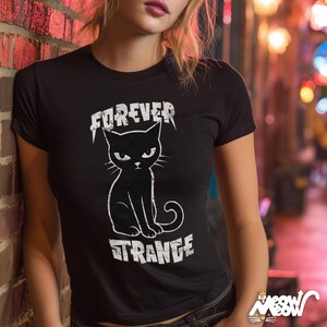 May include: Black t-shirt featuring a white graphic of a cat with the words "FOREVER STRANGE". The cat has an angry expression. The shirt is short-sleeved and made of a soft material.