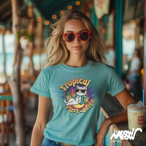 May include: A light blue t-shirt featuring a graphic of a cat wearing sunglasses and a lei, holding a pineapple drink. The graphic says "Tropical Purr-adise".