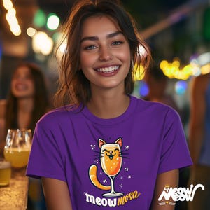 May include: A woman wearing a purple t-shirt with a cartoon cat holding a glass of mimosa. The shirt says "Meowmosa".