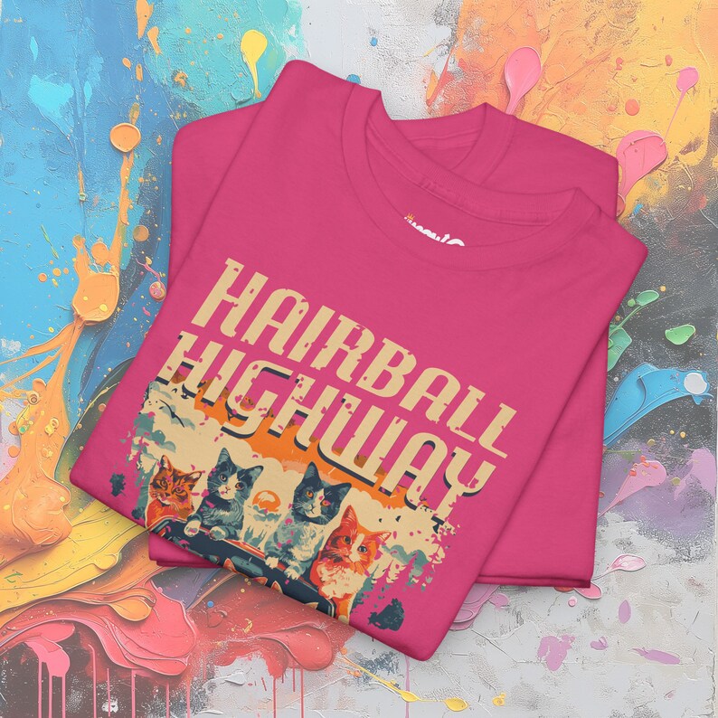 Op de afbeelding: Roze T-shirt met een retro-grafiek van katten die een auto rijden. De grafiek zegt "Hairball Highway".