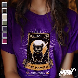 May include: Purple t-shirt with a black cat illustration on a tarot card design. The card reads "IX The Zoomies" and "Channel your chaos, embrace the feline frenzy".